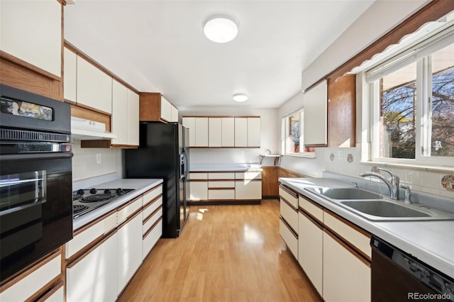 kitchen featuring white cabinets, black appliances, sink, backsplash, and light hardwood / wood-style flooring