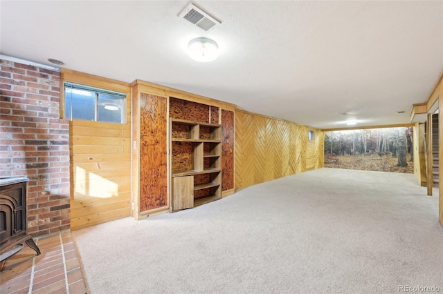 unfurnished living room featuring a wood stove, carpet, and wooden walls