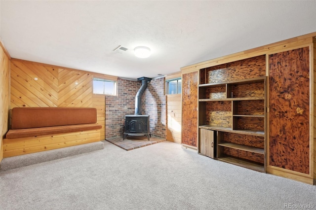 unfurnished living room featuring wood walls, a wood stove, and carpet flooring