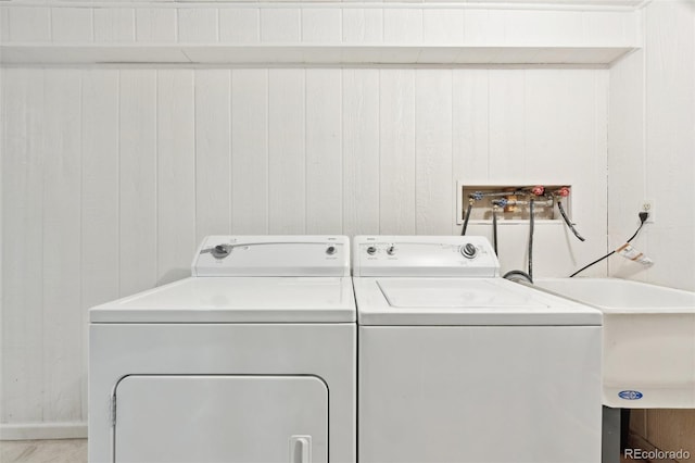 laundry area featuring wood walls, sink, and separate washer and dryer