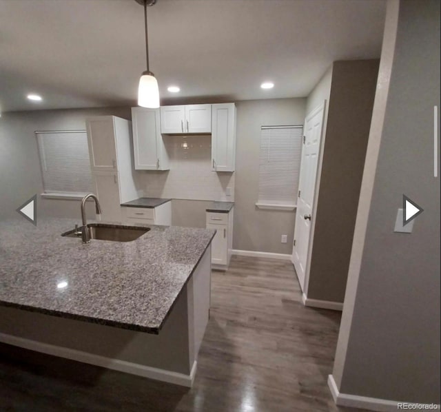 kitchen featuring dark wood-type flooring, pendant lighting, white cabinetry, dark stone counters, and sink