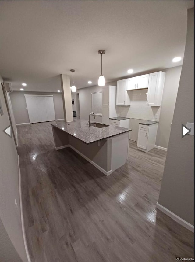 kitchen featuring a kitchen island with sink, wood-type flooring, white cabinets, decorative light fixtures, and sink