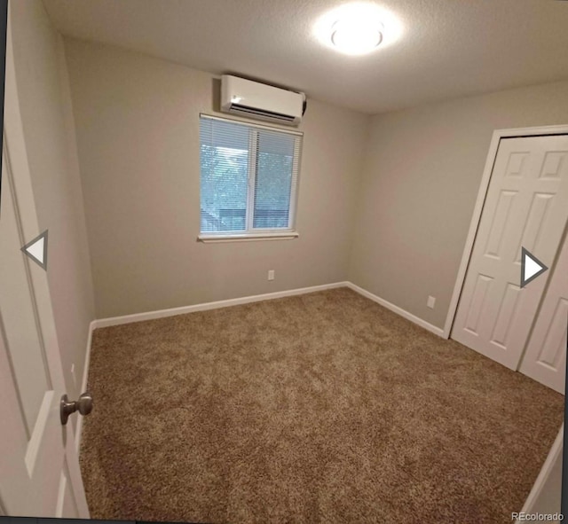 spare room featuring a textured ceiling, a wall mounted AC, and carpet