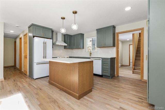 kitchen with pendant lighting, wall chimney range hood, white appliances, a center island, and light wood-type flooring