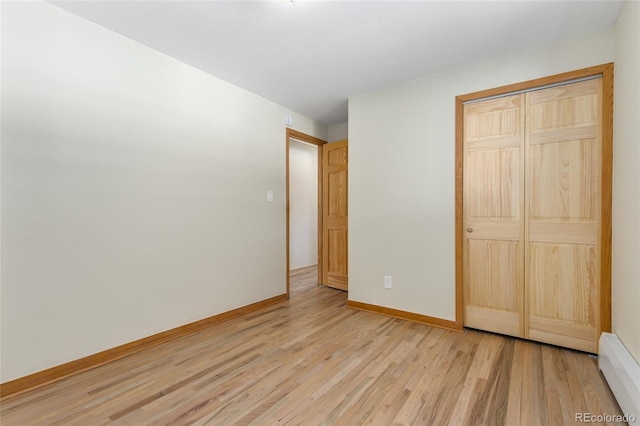 unfurnished bedroom featuring a closet, baseboards, light wood-style floors, and a baseboard radiator