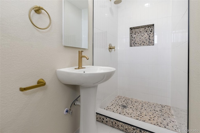 bathroom featuring a textured wall and tiled shower