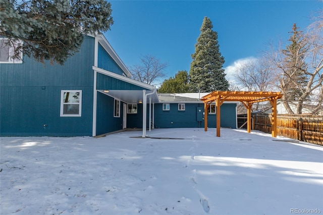 snow covered back of property featuring fence and a pergola