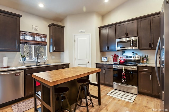 kitchen with sink, appliances with stainless steel finishes, butcher block counters, dark brown cabinetry, and light wood-type flooring