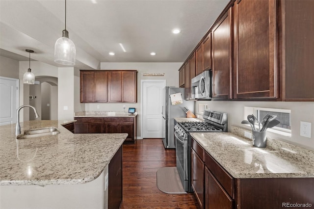 kitchen featuring a sink, stainless steel appliances, arched walkways, light stone countertops, and hanging light fixtures