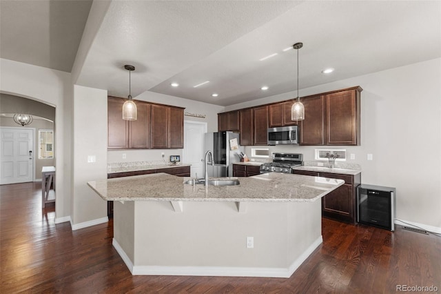 kitchen featuring decorative light fixtures, stainless steel appliances, arched walkways, wine cooler, and a kitchen island with sink