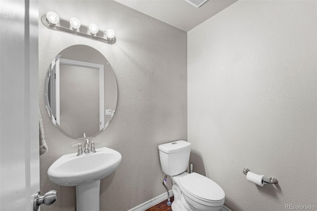 half bathroom with baseboards, a textured wall, and toilet