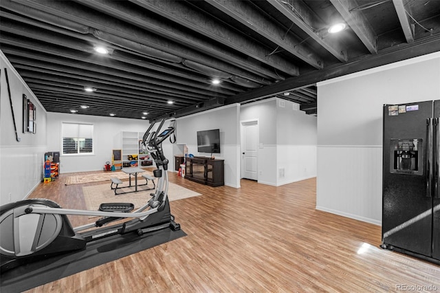 exercise area featuring light wood-type flooring and a wainscoted wall