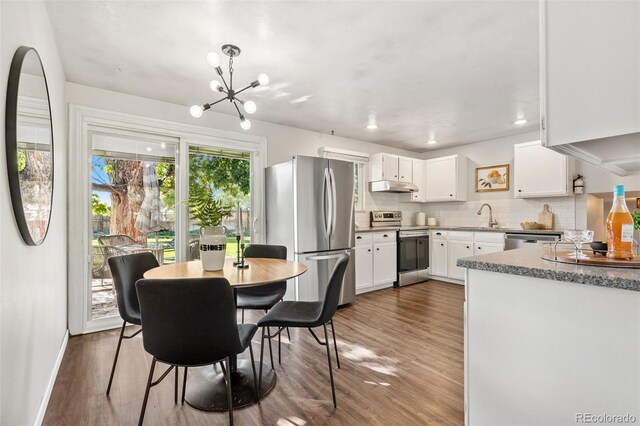 7565 Newland St, Arvada, CO 80003 - kitchen featuring appliances with stainless steel finishes, under cabinet range hood, wood finished floors, white cabinets, and a chandelier