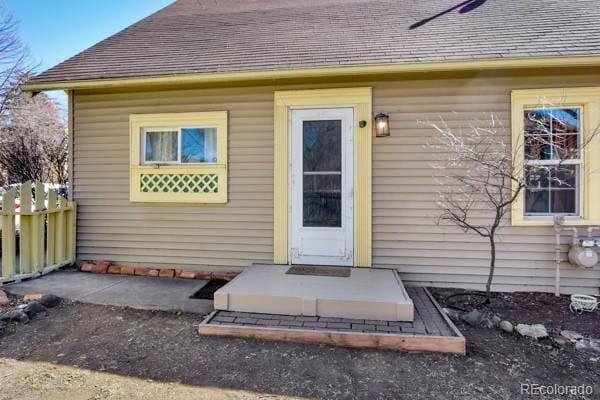 doorway to property featuring a shingled roof and fence