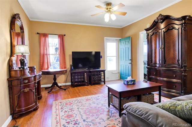 living room featuring crown molding, light wood-style flooring, baseboards, and ceiling fan