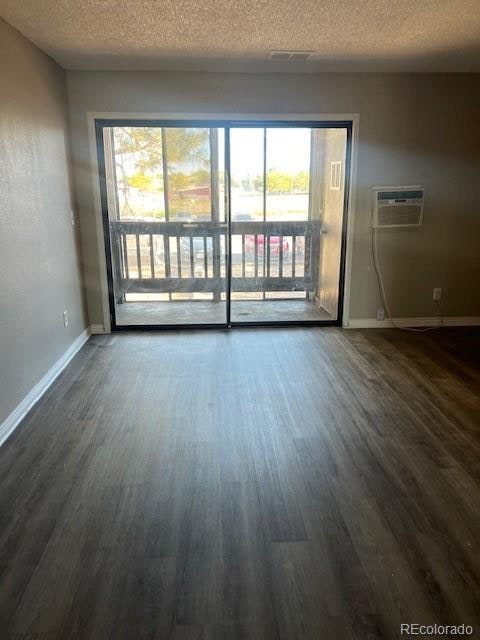 empty room featuring dark wood-type flooring, a wall mounted AC, and a textured ceiling