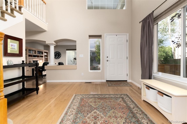 entryway featuring arched walkways, decorative columns, light wood finished floors, and a high ceiling