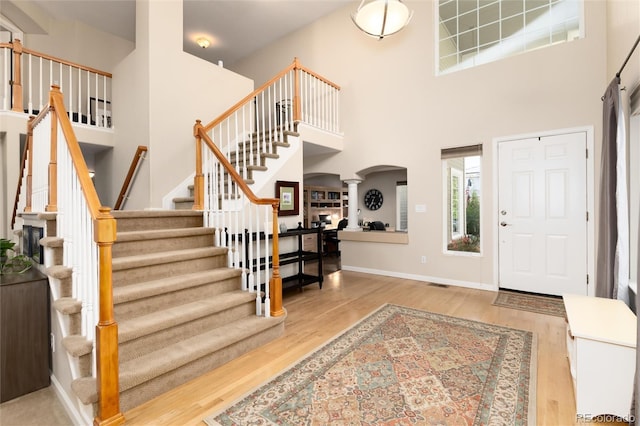 entrance foyer featuring arched walkways, wood finished floors, a towering ceiling, ornate columns, and stairway