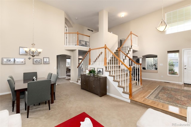 carpeted dining room featuring a high ceiling, a notable chandelier, arched walkways, stairs, and baseboards