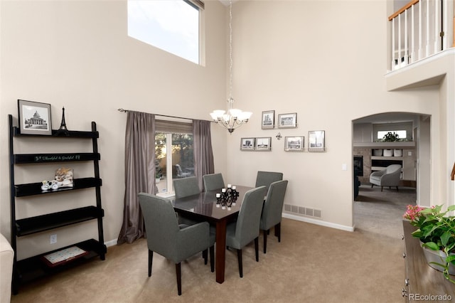 dining space featuring a fireplace, carpet floors, a chandelier, a towering ceiling, and visible vents
