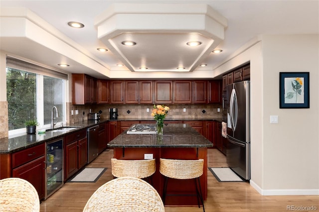 kitchen with wine cooler, tasteful backsplash, a sink, light wood-style flooring, and stainless steel appliances