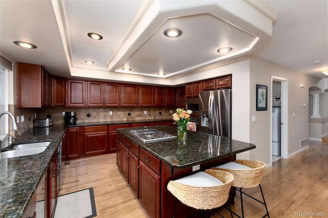 kitchen with a sink, light wood finished floors, a breakfast bar area, stainless steel appliances, and decorative backsplash