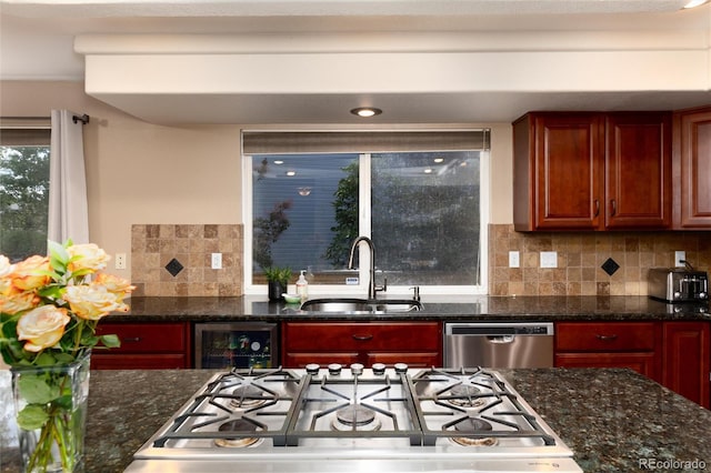kitchen with beverage cooler, a sink, dark stone countertops, appliances with stainless steel finishes, and backsplash