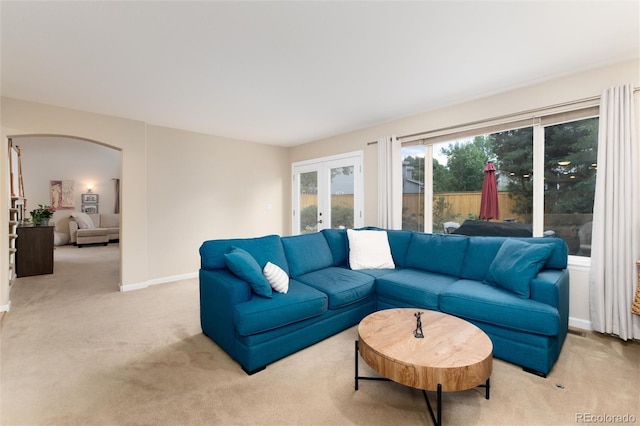 living room with arched walkways, baseboards, french doors, and light colored carpet