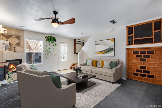 carpeted living room featuring ceiling fan, a fireplace, and a textured ceiling