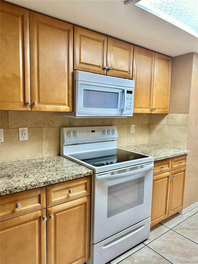 kitchen with white appliances, light stone counters, light tile patterned floors, and backsplash