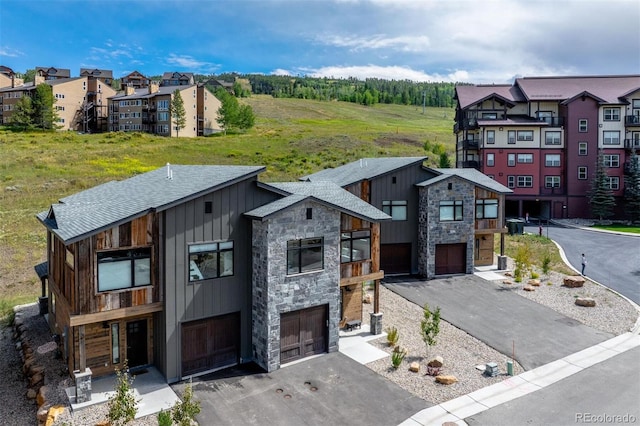 contemporary house with driveway, stone siding, board and batten siding, and an attached garage