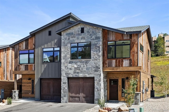 contemporary home featuring a garage, stone siding, board and batten siding, and concrete driveway