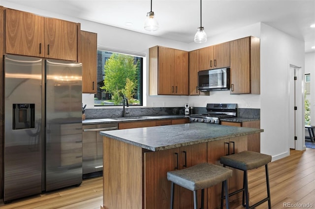 kitchen with sink, a center island, hanging light fixtures, appliances with stainless steel finishes, and light wood-type flooring