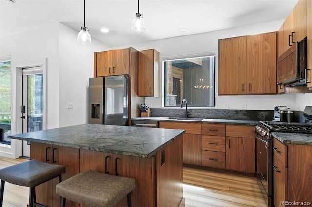 kitchen featuring a kitchen bar, light wood-type flooring, sink, black appliances, and decorative light fixtures