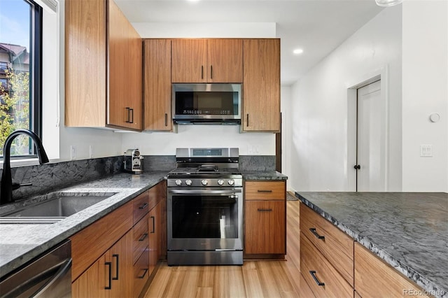 kitchen featuring light wood-type flooring, sink, appliances with stainless steel finishes, and dark stone counters