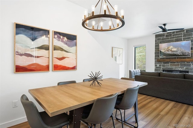 dining space with a fireplace, wood-type flooring, and ceiling fan with notable chandelier