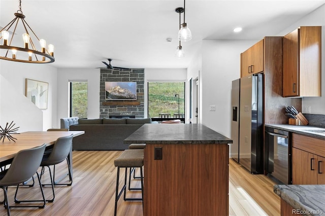 kitchen with ceiling fan with notable chandelier, light wood-type flooring, decorative light fixtures, and appliances with stainless steel finishes