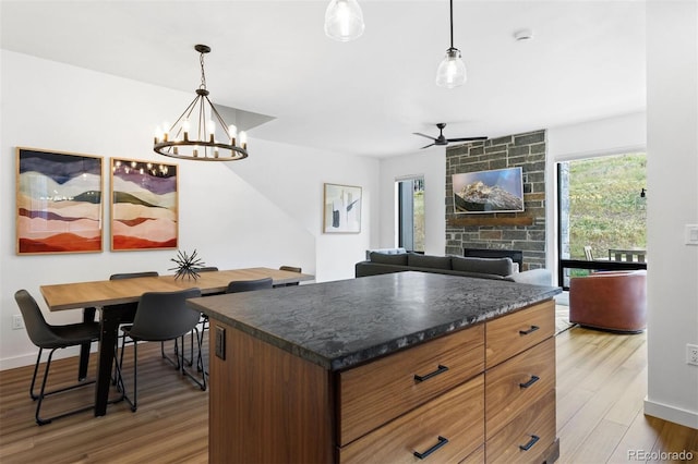 kitchen featuring hardwood / wood-style flooring, a center island, a stone fireplace, and hanging light fixtures