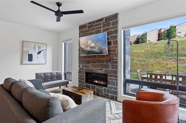 living room featuring ceiling fan, a stone fireplace, and wood-type flooring