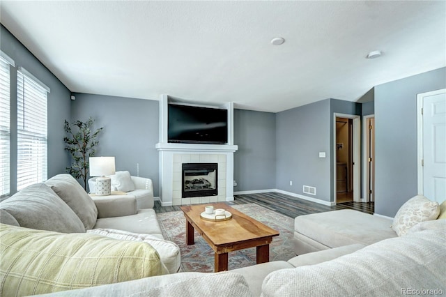 living room with baseboards, a fireplace, visible vents, and wood finished floors