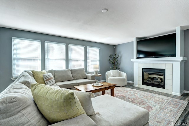 living area with a tile fireplace, baseboards, and wood finished floors