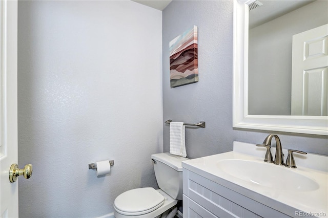 bathroom with toilet, a textured wall, vanity, and visible vents