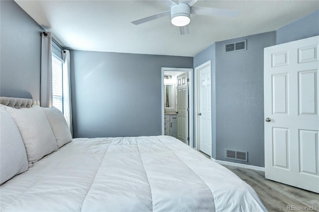 bedroom with ensuite bathroom, light wood finished floors, visible vents, and a ceiling fan