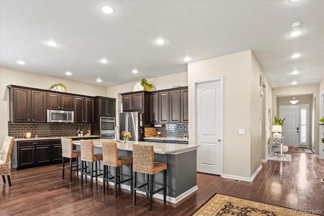 kitchen with appliances with stainless steel finishes, a center island with sink, a breakfast bar area, decorative backsplash, and recessed lighting