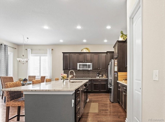 kitchen with stainless steel appliances, a sink, dark wood-type flooring, a kitchen island with sink, and a breakfast bar