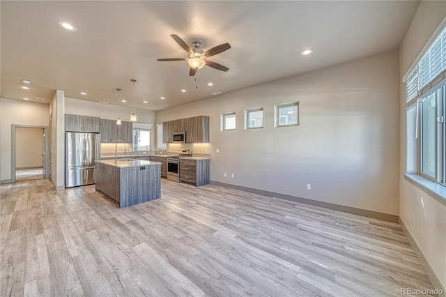 kitchen with sink, light stone counters, appliances with stainless steel finishes, a kitchen island, and pendant lighting