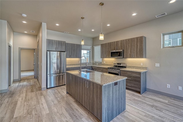 kitchen featuring hanging light fixtures, stainless steel appliances, a center island, light stone countertops, and light wood-type flooring