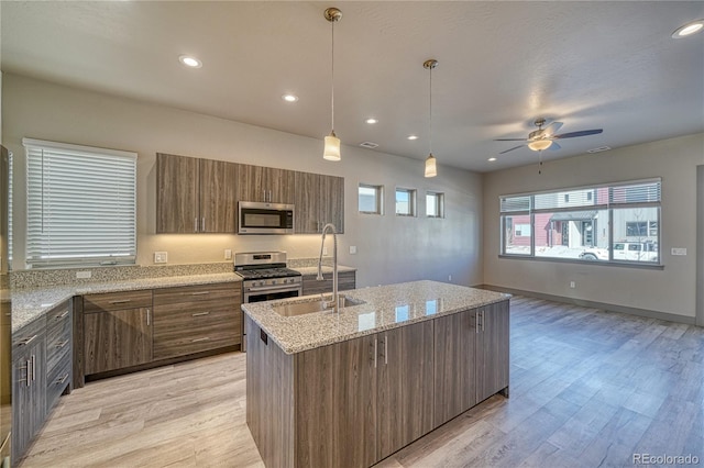 kitchen featuring sink, a kitchen island with sink, stainless steel appliances, light stone countertops, and light hardwood / wood-style floors