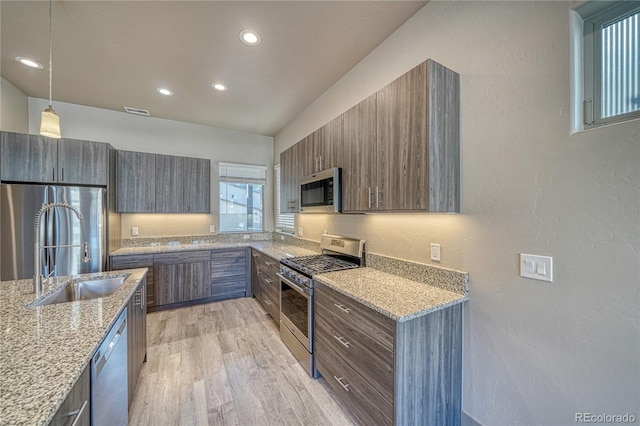 kitchen with decorative light fixtures, sink, light stone counters, stainless steel appliances, and light hardwood / wood-style flooring