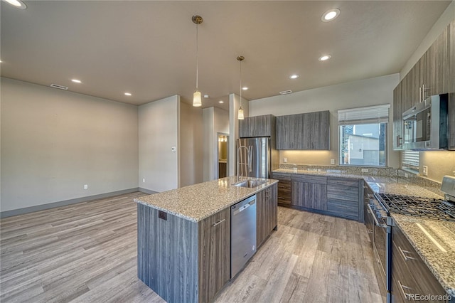 kitchen with sink, decorative light fixtures, light wood-type flooring, appliances with stainless steel finishes, and an island with sink